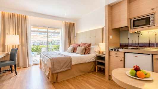 Et hotelværelse med en stor seng, skrivebord og køkken samt en balkon med udsigt. (AI-genereret tekst)