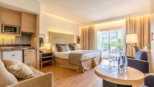 Hotelværelse med dobbeltseng, siddeområde og køkken, samt altan med udsigt. (AI-genereret tekst)