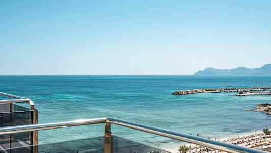 Udsigt fra en altan over havet og en strand med parasoller. (AI-genereret tekst)