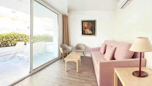 Sofa med pink betræk, sofabord, to stole og vindue med udsigt til terrassen. (AI-genereret tekst)