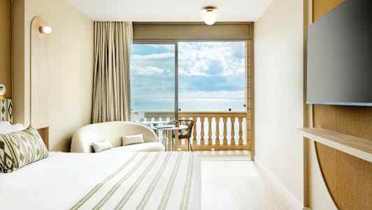 Et hotelværelse med havudsigt fra balkonen. Et stort vindue vender ud mod havet. (AI-genereret tekst)