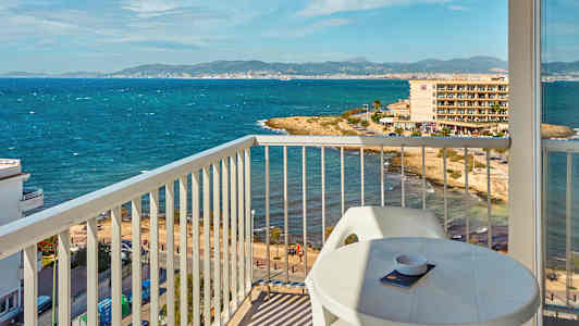 Udsigt fra en balkon mod en kyst med hav og bygninger i baggrunden. (AI-genereret tekst)