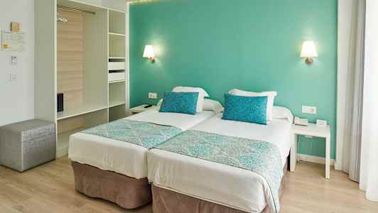 Et hotelværelse med to enkeltsenge, turkise puder og vægge. (AI-genereret tekst)