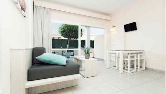 Et moderne lyst rum med siddepladser, bord og en plante, store vinduer og udsigt til have. (AI-genereret tekst)