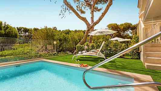 Udendørs pool med liggestole og parasoller samt grønt i baggrunden. (AI-genereret tekst)