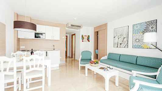 Billedet viser en lys og moderne møbleret stue med tekøkken og spiseplads. (AI-genereret tekst)