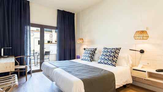 Et hotelværelse med en dobbeltseng, blåpude og natlamper. Et skrivebord med stol står ved siden af, samt en altan med bord og stole. (AI-genereret tekst)