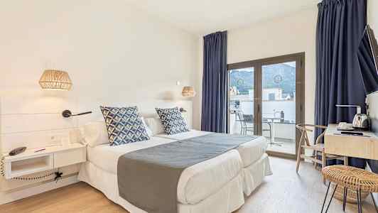 Et hotelværelse med to enkeltsenge, blå dekorationspuder, skrivebord og en altan med udsigt. (AI-genereret tekst)