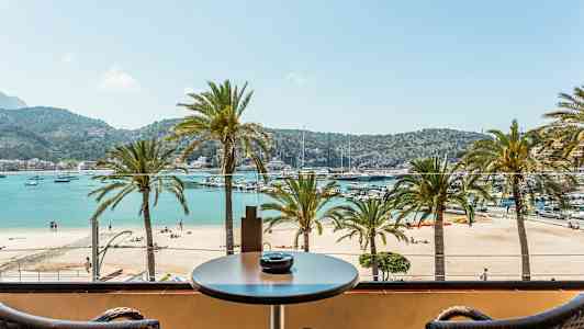 Udsigt fra en balkon mod en strand med palmer og hav på en solrig dag. (AI-genereret tekst)