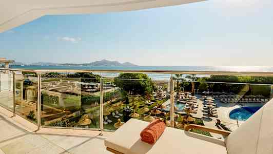 Udsigt fra balkon med liggestole og pool, med strand og bjerge i baggrunden. (AI-genereret tekst)