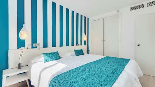 Et soveværelse med en seng, blåstribet væg og hvide møbler. (AI-genereret tekst)