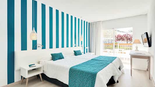 Et moderne hotelværelse med stribet væg, hvidt og turkis sengetøj samt en balkon med udsigt. (AI-genereret tekst)