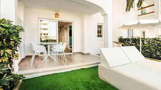 Udendørs terrasse med bord og stole samt liggestole og parasol ved græsplæne. (AI-genereret tekst)