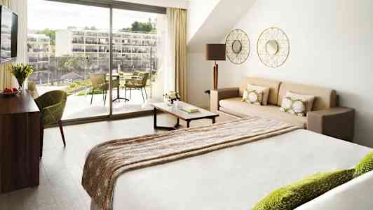 Et lyst hotelværelse med en seng, en sofa og en balkon udenfor. (AI-genereret tekst)