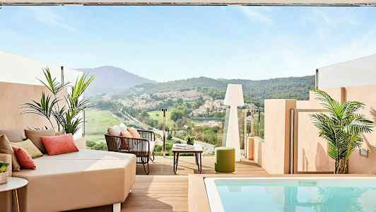 En terrasse med udsigt over en grøn dal og huse i det fjerne, med siddepladser og en lille pool. (AI-genereret tekst)