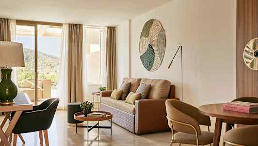 Stue med sofa, sofabord, spisebord og stole samt udsigt gennem store vinduer til naturen. (AI-genereret tekst)