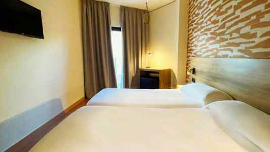 To enkeltsenge på et hotelværelse med et mønstret hovedgærde og et tv på væggen. (AI-genereret tekst)