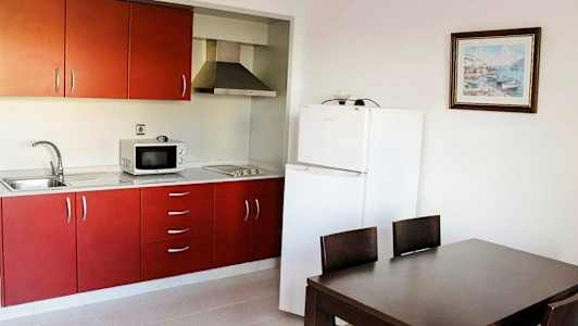 Et køkken med røde skabe, et køleskab og en spiseplads med et bord og stole. (AI-genereret tekst)