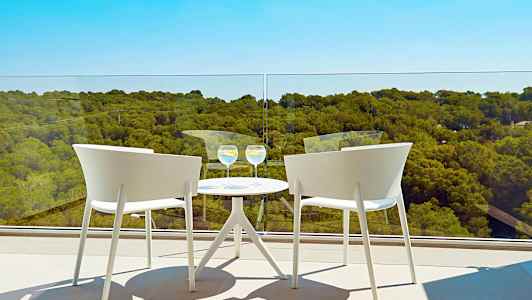 To hvide stole ved et rundt bord med to glas på en altan med udsigt over et skovklædt landskab. (AI-genereret tekst)