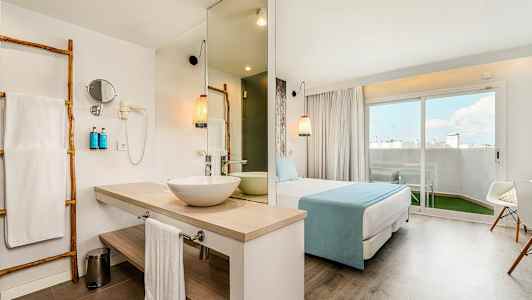Hotelværelse med badeområde, sovemiljø og siddeafdeling. Stor terrassedør ud til en udendørs terrasse. (AI-genereret tekst)