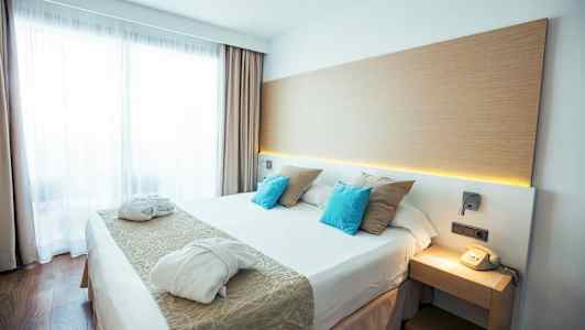 Et moderne hotelværelse med en dobbeltseng, to badekåber og en telefon på natbordet. (AI-genereret tekst)