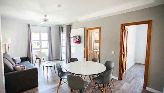 En stue med grå sofa, spisebord med stole og et TV på væggen. (AI-genereret tekst)