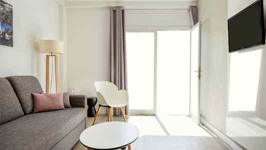 En lys og moderne indrettet stue med grå sofa, en hvid stol og et rundt sofabord. (AI-genereret tekst)