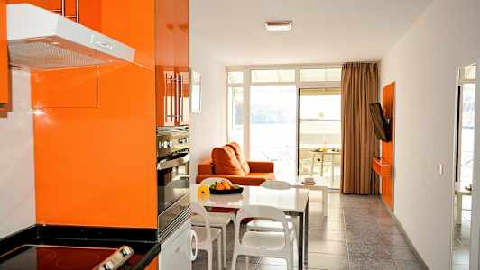 Moderne køkken og stue med orange indretning og udsigt til havet. (AI-genereret tekst)