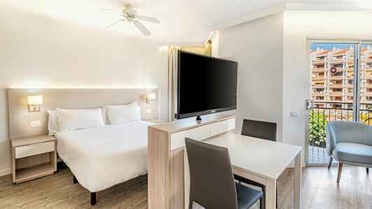 Lyst soveværelse med en dobbeltseng, et bord med stole og et stort tv foran sengen. (AI-genereret tekst)