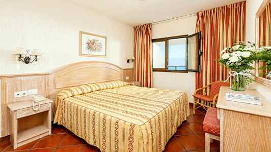 Et hotelværelse med en dobbeltseng, natbord og vindue med havudsigt. (AI-genereret tekst)