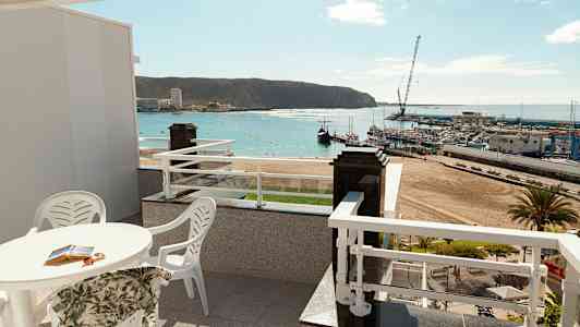 Terrasse med udsigt over en strand og en havn. (AI-genereret tekst)