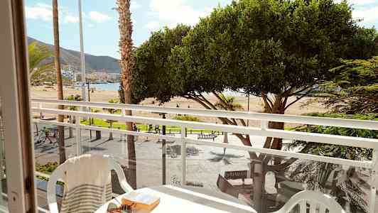 Udsigt fra en altan mod en strand med palmer og træer. (AI-genereret tekst)