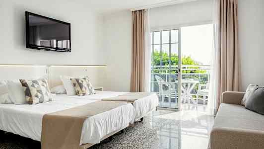 Hotelværelse med dobbeltseng, sofa, vægmonteret TV og balkon med møbler. (AI-genereret tekst)