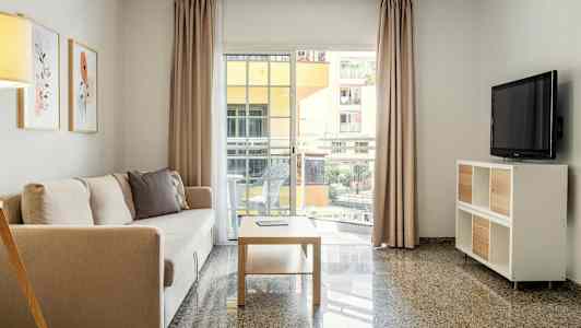 En stue med en sofa, et sofabord og et tv samt store vinduer ud til en altan. (AI-genereret tekst)