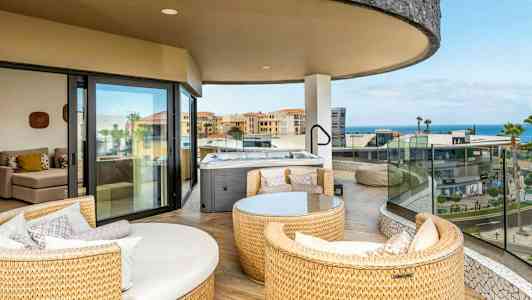 En rummelig altan med siddepladser og en jacuzzi, udsigt over bygninger og hav. (AI-genereret tekst)