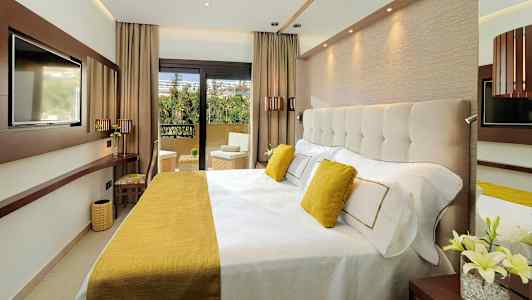 Et moderne hotelværelse med en bred seng, indrettet med gule detaljer og udsigt til en balkon. (AI-genereret tekst)