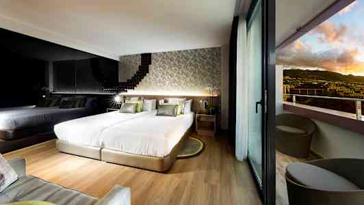 Moderne hotelværelse med to senge, en spejlvæg og balkon med udsigt over landskabet. (AI-genereret tekst)