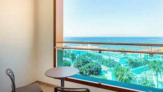 En altan med bord og stole, udsigt over havet og hotelområde. (AI-genereret tekst)