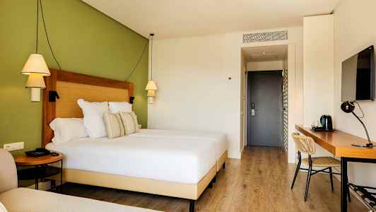 Hotelværelse med en bred seng, skrivebord og grøn væg. (AI-genereret tekst)