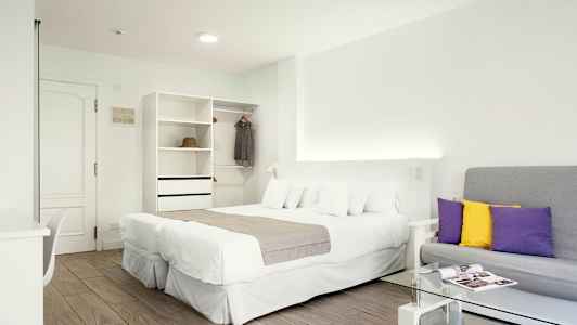 Et lyst hotelværelse med en dobbeltseng, en sofa og et garderobeskab. (AI-genereret tekst)