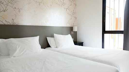 Et hotelværelse med to enkelt senge og et natbord. (AI-genereret tekst)