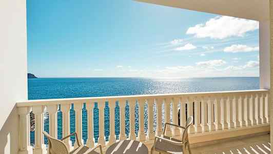 Udsigt fra en balkon med bord og stole mod havet. (AI-genereret tekst)