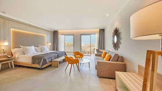 Et moderne hotelværelse med dobbeltseng, siddeområde med orange stole, en sofa og en balkon med udsigt til havet. (AI-genereret tekst)