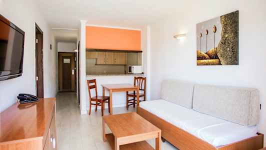 Lejlighedsinteriør med en sofa, et bord, to stole og et åbent køkken med orange væg. (AI-genereret tekst)