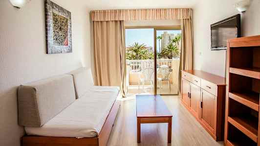 Et møbleret rum med en sofa, et bord, en TV og en hylde. Udgang til en altan med siddepladser. (AI-genereret tekst)