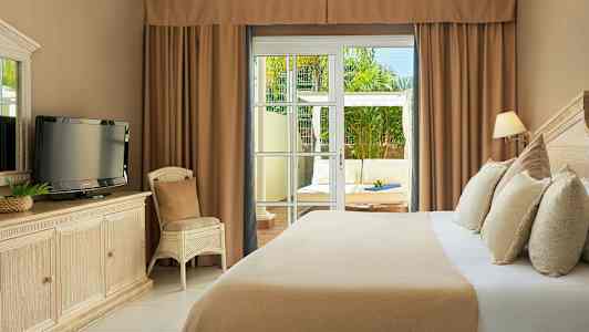 Et hotelværelse med en seng, et TV på en kommode og en stol. Glasdøre fører til en terrasse med siddepladser. (AI-genereret tekst)