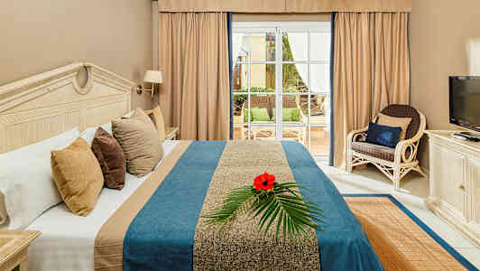 Billede af et hotelværelse med en seng, et TV og udsigt til en terrasse. (AI-genereret tekst)