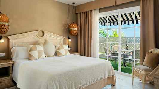 Et hotelværelse med en stor seng, smagfuldt interiør og vinduer ud til en balkon med udsigt. (AI-genereret tekst)