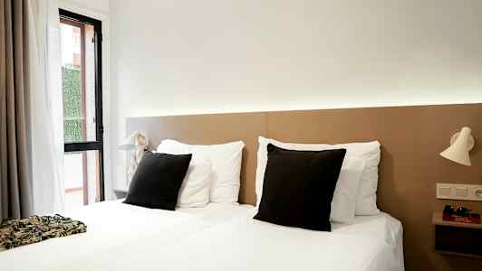 Et hotelværelse med to enkeltsenge, hvidt sengetøj og sorte puder, samt lyse natlamper på væggen. (AI-genereret tekst)