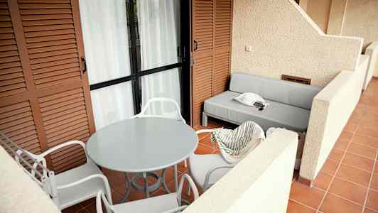 En rummelig terrasse med hvide stole rundt om et rundt bord og en grå sofa. (AI-genereret tekst)